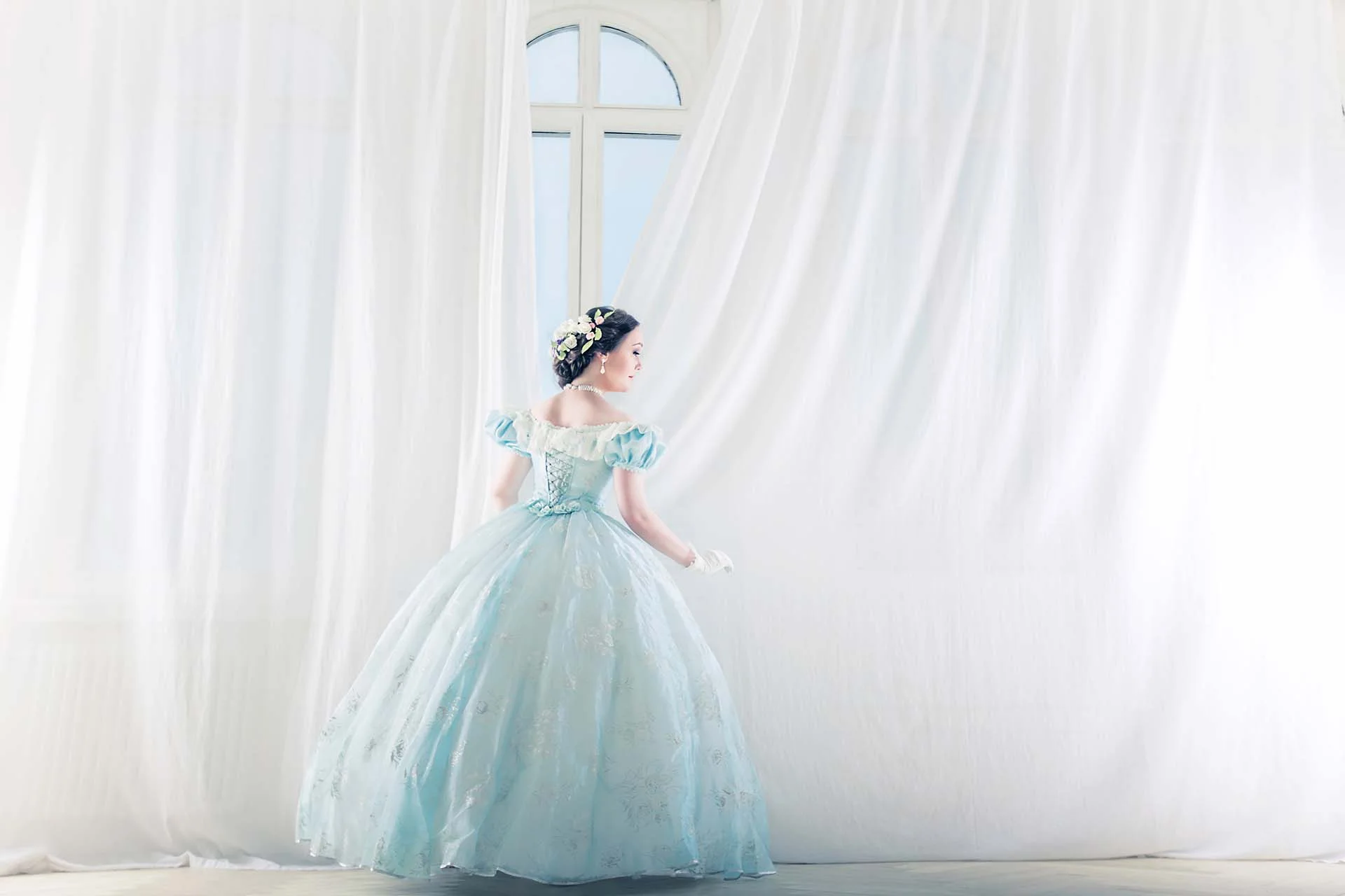Elegant woman in Ball Gown Wedding Dress straightens the curtains